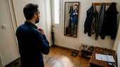 Ένας Έλληνας στέκεται μπροστά στον καθρέφτη του σπιτιού του και κουμπώνει το πουκάμισό του.